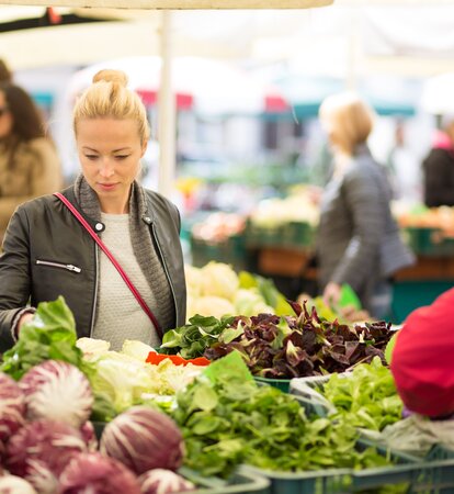 Eine Frau steht vor einem Marktstand und sucht sich Gemüse aus. 