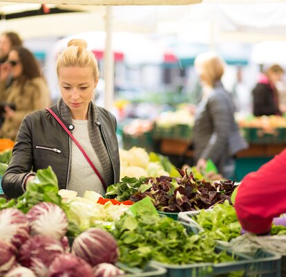 Eine Frau steht vor einem Marktstand und sucht sich Gemüse aus. 