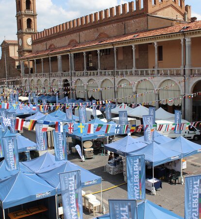 Three blue gazebos in a row are standing on a town square. The flags of different nations are 