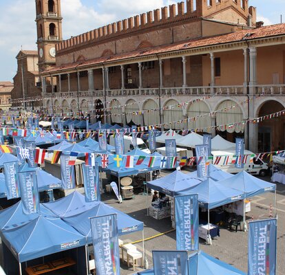 Three blue gazebos in a row are standing on a town square. The flags of different nations are 