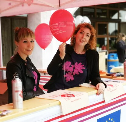 Cora Cavicchi steht mit einer Mitarbeiterin im Faltpavillon bei einer Veranstaltung. In der Hand hält sie einen Luftballon.