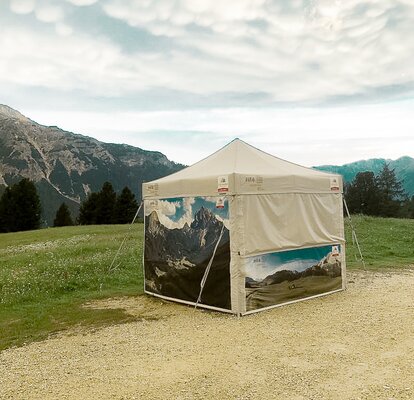 Ein Faltpavillon von MASTERTENT, bedruckt mit Fotos vom Pragser Wildsee, steht auf einer Wiese.