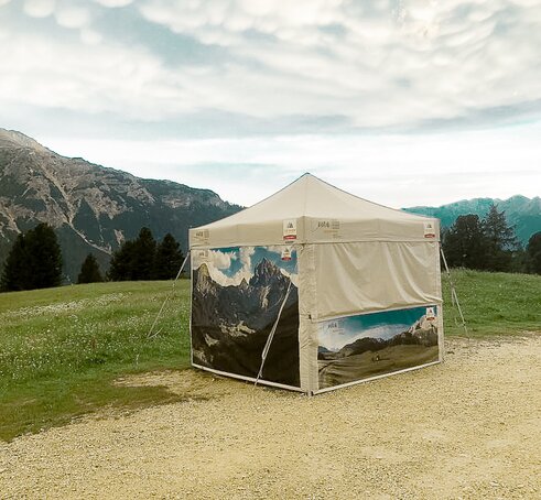 Un gazebo pieghevole MASTERTENT personalizzato con delle foto del lago di Braies su un prato.