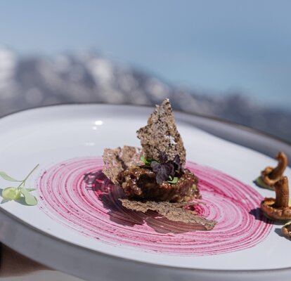 Hauptspeise aus Lamm, Goldbrasse, Urkarotte und Caponata im Rahmen von Südtirol kocht am Schnalstaler Gletscher. Dahinter sieht man das Bergpanorama.