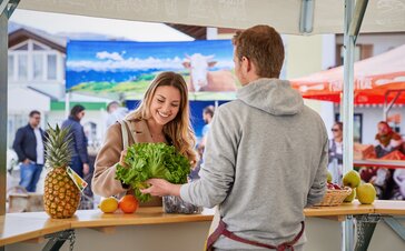 Il venditore sta spiegando alla sua cliente i suoi prodotti e le mostra un insalata. 