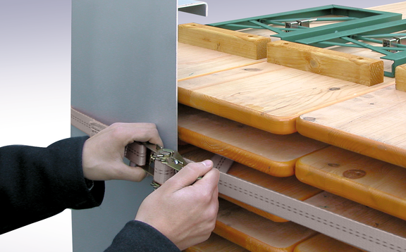 A person who tightens a strap of a transport box with tables and beches can be seen