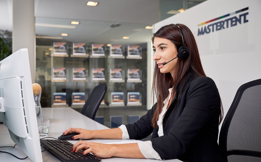 Una empleada con un headset está sentada delante de un ordenador, hablando con un cliente al teléfono.