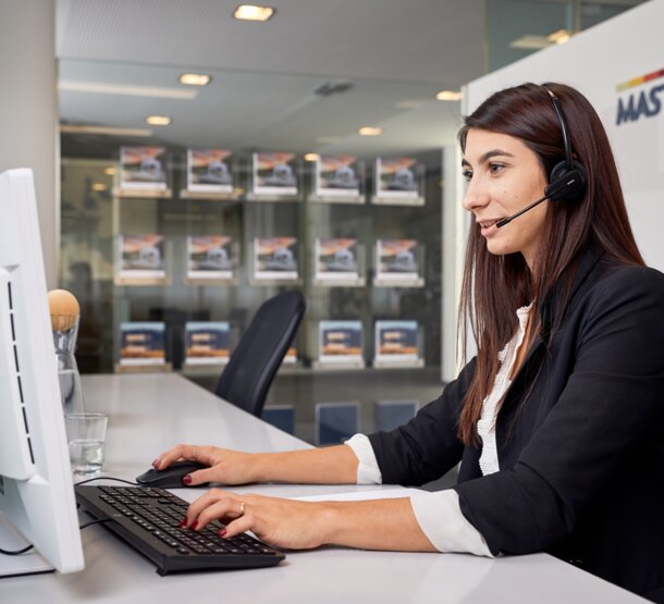 Un angajat stă în fața PC-ului cu o cască și oferă asistență clientului la telefon.