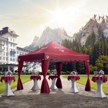 Gazebo pieghevole rosso elegante con frontalino ondulato e copripali davanti ad un albergo. Sotto si trovano dei tavoli alti.