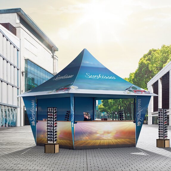 A promotion tent for sunglasses is located in the shopping street. The gazebo is blue and printed all over. 