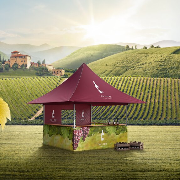 A red gazebo with four awnings is located in the middle of the vines. The sidewalls are printed with vines. In front of the gazebo two boxes with wine bottles are situated. 