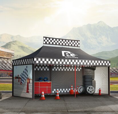 Black gazebo next to the race track. The gazebo is printed with racing patterns. Below them are tyres, cones and other motorsport accessories.