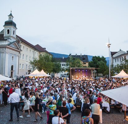 Faltpavillons mit Vordach beim Dine, Wine and Music auf dem Domplatz in Brixen. Die Gäste genießen den Abend. Im Hintergrund sieht man die Band auf der Bühne.