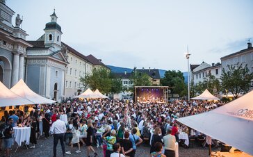 Diversi gazebo per eventi nella piazza del Duomo di Bressanone al Dine & Wine festival. La gente è seduta e festeggia.