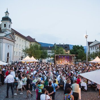 Diversi gazebo per eventi nella piazza del Duomo di Bressanone al Dine & Wine festival. La gente è seduta e festeggia.