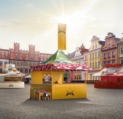 Ein Marktstand von Mastertent steht in der Mitte eines Platzes. Der Marktstand mit Vordach hat eine Theke und Seitenwände halber Höhe. Er ist bedruckt und fällt auf. 