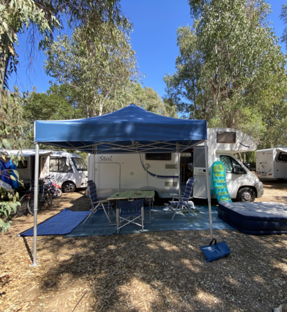 Blaues Campingzelt 3x3 m steht vor dem Wohnwagen auf dem Campingplatz. Darunter stehen ein Tisch mit Stühlen.