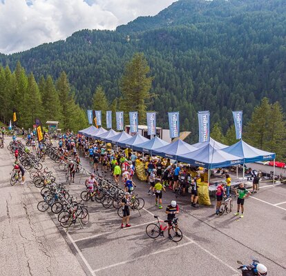 Blaue Faltpavillons mit einer Fahne auf dem Dach sind nebeneinander aufgereiht beim Ötztaler Radmarathon. Durch die Verbindung ergibt sich ein Baukastensystem bei Events.