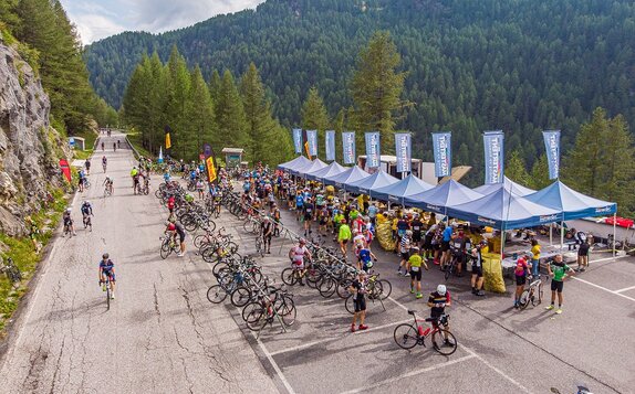 Blaue Faltpavillons mit einer Fahne auf dem Dach sind nebeneinander aufgereiht beim Ötztaler Radmarathon. Durch die Verbindung ergibt sich ein Baukastensystem bei Events.