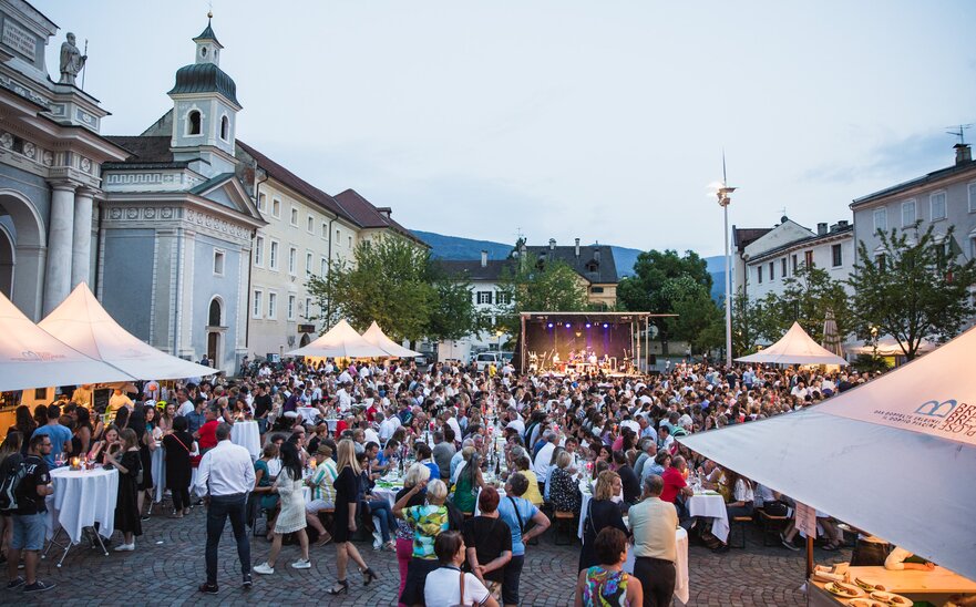 Diversi gazebo per eventi bianchi 3x3 m con tettoie nella piazza del Duomo di Bressanone al Dine & Wine festival. La gente è seduta e festeggia. Gazebo per associazioni e comuni.