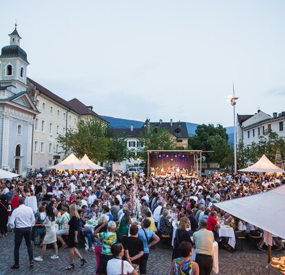 Several gazebos on the Brixen Dome Square at the Dine & Wine Festival. People are sitting and celebrating.