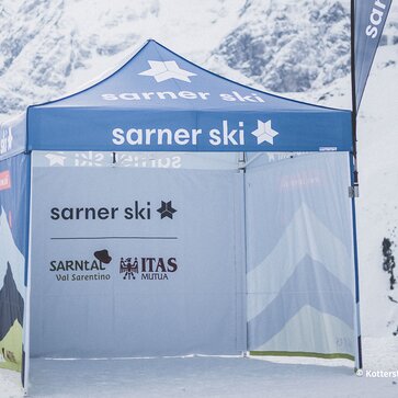 Il gazebo promozionale di Sarner Ski, completamente stampato, in mezzo alle montagne innevate. Ha le pareti laterali stampate e una bandiera pubblicitaria. | © Kottersteger Manuel