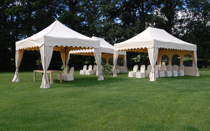 Tre gazebo pieghevoli bianche sul prato. Sotto i gazebo pieghevoli ci sono delle sedie con delle coperture. 