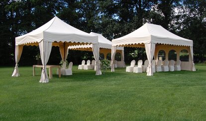 Tre gazebo pieghevoli bianche sul prato. Sotto i gazebo pieghevoli ci sono delle sedie con delle coperture. 