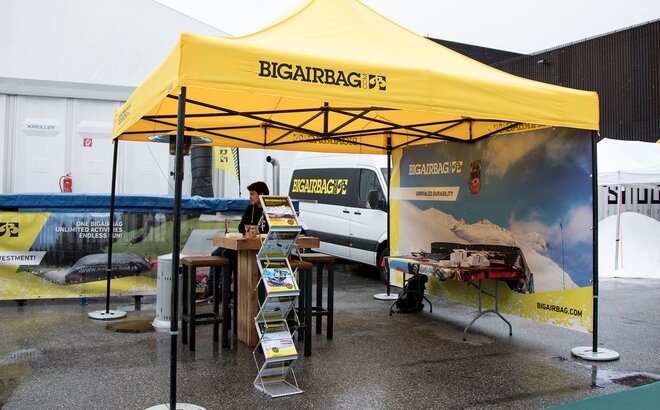 The yellow exhibition tent from Bigairbag is located at the outdoor fairground. The gazebo consists of a yellow roof with black structure. A seller is sitting below the gazebo. 