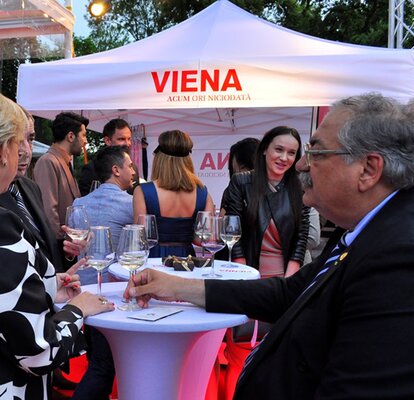 Weißes Partyzelt mit der Aufschrift "Viena" steht im Hintergrund. Davor befinden sich die Gäste und trinken Prosecco.