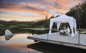 Gazebo pieghevole bianco con copripali sul molo. Le quattro presone cenano sotto il gazebo durante il tramonto. 