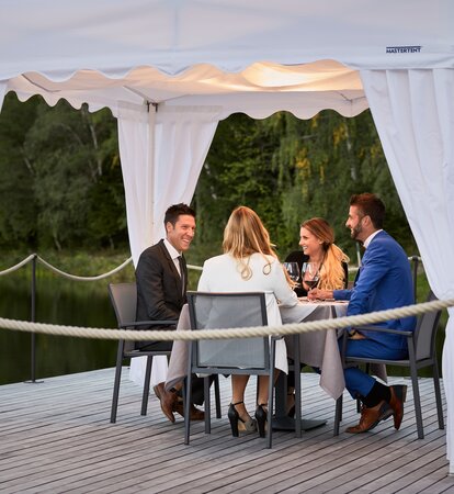 Die 4 Gäste sitzen unter dem Faltpavillon beim Abendessen.