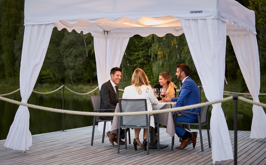 4 guests are sitting under the gazebo. They are having dinner. 