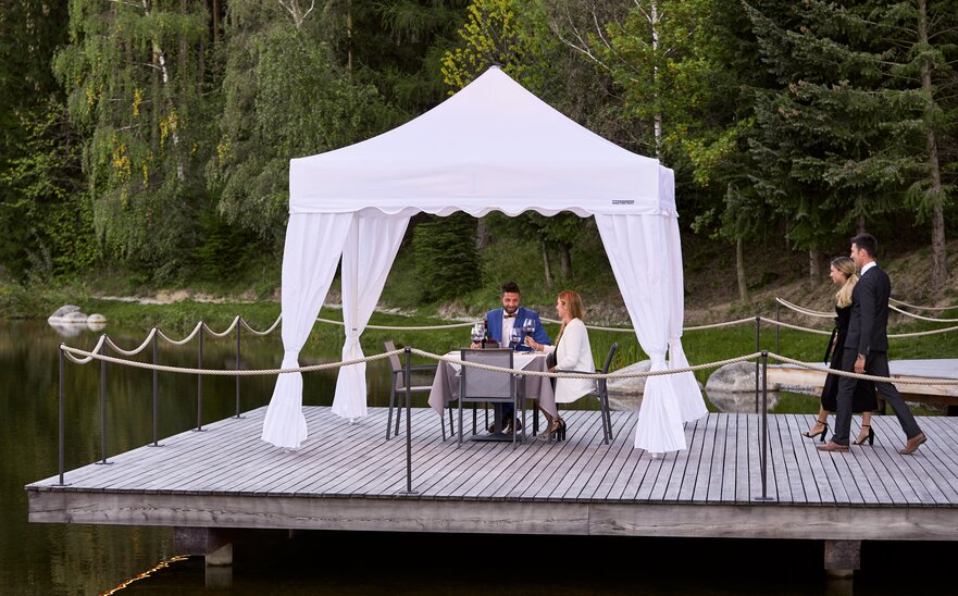 One couple is sitting under the gazebo. The second couple is approaching. Everything is prepared for dinner. 