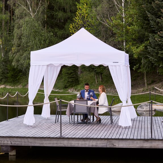 One couple is sitting under the gazebo. The second couple is approaching. Everything is prepared for dinner. 