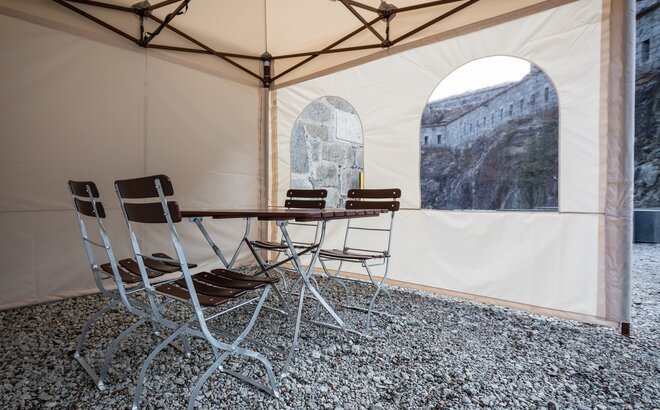 Il gazebo pieghevole visto dall´interno. Ci sono un tavolo e due sedie all´interno della tenda. Si vede la parete laterale con finestra.