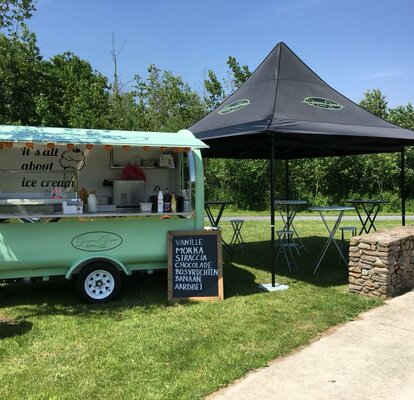 Der Street Food Stand von "Dingenen & Dergent" steht auf einer Wiese. Der türkisfarbene Anhänger steht neben dem schwarzen Faltpavillon.