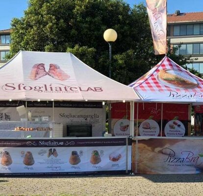 Ein Streetfood Stand mit zwei Faltpavillons mit Vordach und einer Fahne auf der Dachspitze. Beide Faltpavillons sind vollflächig bedruckt.