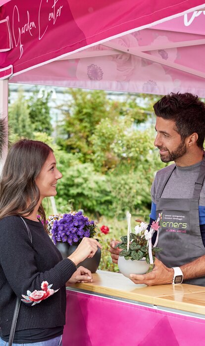 Un cliente sta parlando con un commesso della giardineria sotto ad un gazebo rosa con tettoia