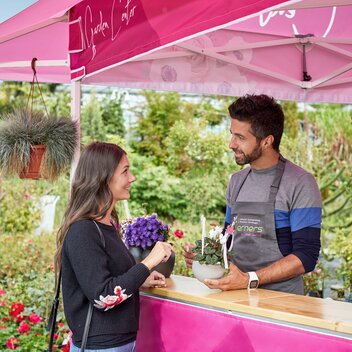 Un cliente sta parlando con un commesso della giardineria sotto ad un gazebo rosa con tettoia