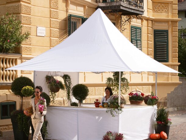 The market stand for flowers is white and has four awinings on all sides. The customer is leaving the gazebo with a flower in her hand. 