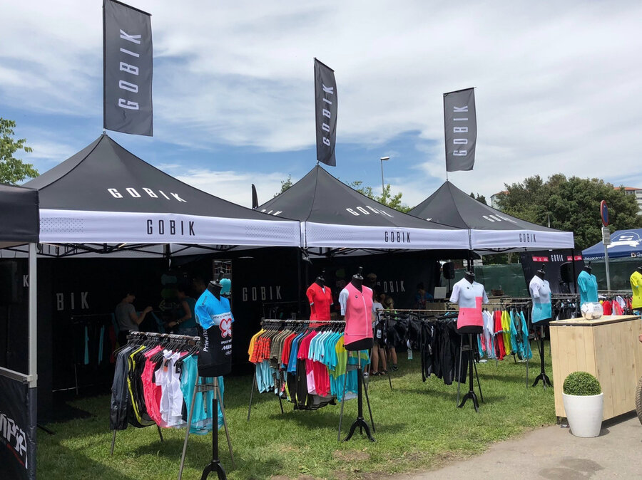 Folding gazebo black 3x3 m customised with logo print, lettering and flags. Black gazebo side walls with white logos and lettering.  Gazebo used as a retail outlet at an event. Retail of T-shirts and sports accessories. 