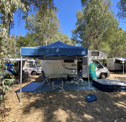 Blaues Campingzelt 3x3 m steht vor dem Wohnwagen auf dem Campingplatz. Darunter stehen ein Tisch mit Stühlen.