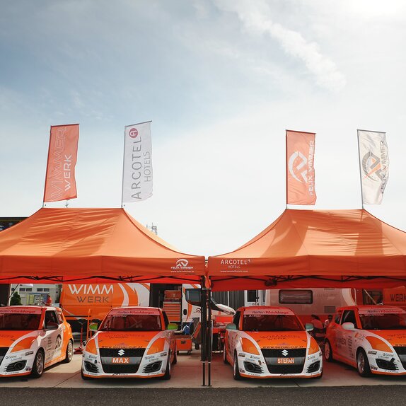 Orange 8x4 gazebo with black frame and two customised flags with Wimmer Werk logo. Paddock gazebo for rally racing cars.