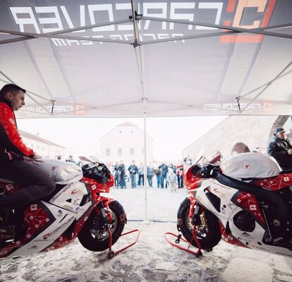 Two red motorcycle racers are standing with their bikes under the gazebo. 