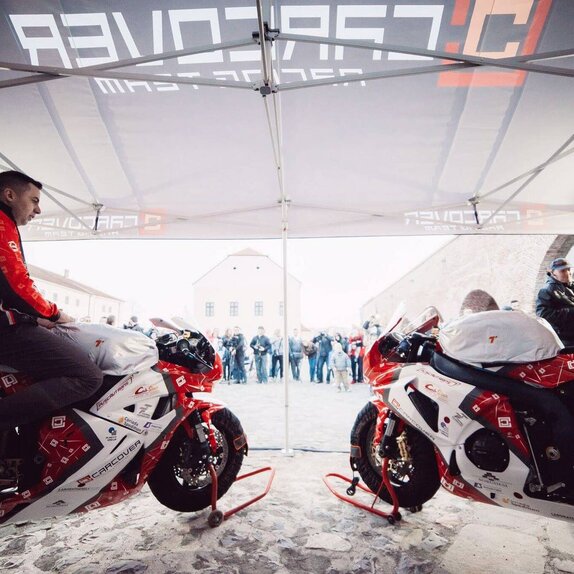 Zwei rote Motorrad-Rennfahrer stehen mit dem Motorrad unter dem Faltpavillon.