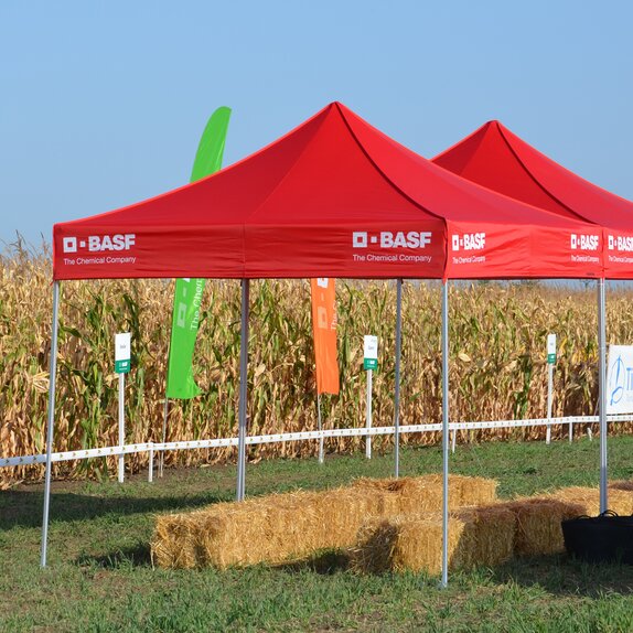 Red gazebo is standing on the field. Below it are some bales of straw. 