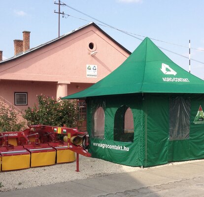 Green agrarian tent equipped with side walls and windows. Next to it there are some agricultural machines.