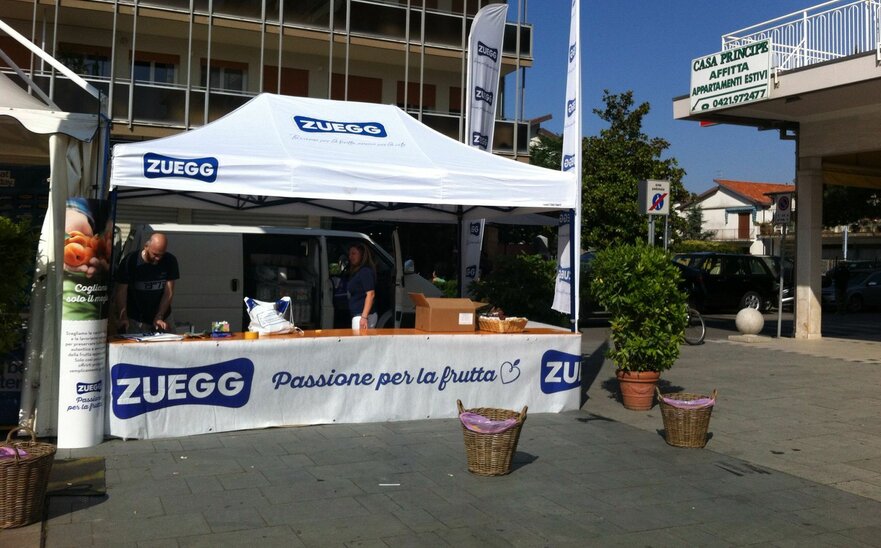 Gazebo pieghevole 4,5x3m bianco personalizzato con logo e pareti laterali a mezza altezza con bancone per stand  Zuegg.