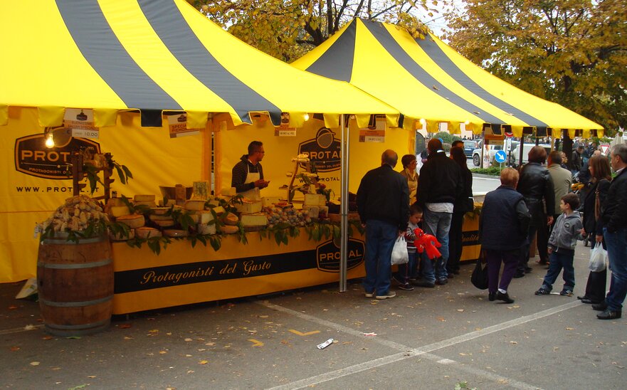 Coppia di gazebo pieghevoli 4,5x3m per la vendita di formaggi di Protal. Tetto con tettoia giallo e nero e frontalino personalizzato su misura a frange. 